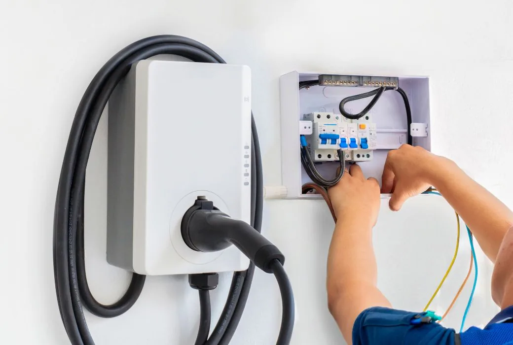 An electrician wiring a charge point circuit into a consumer unit beside a wall-mounted EV charger